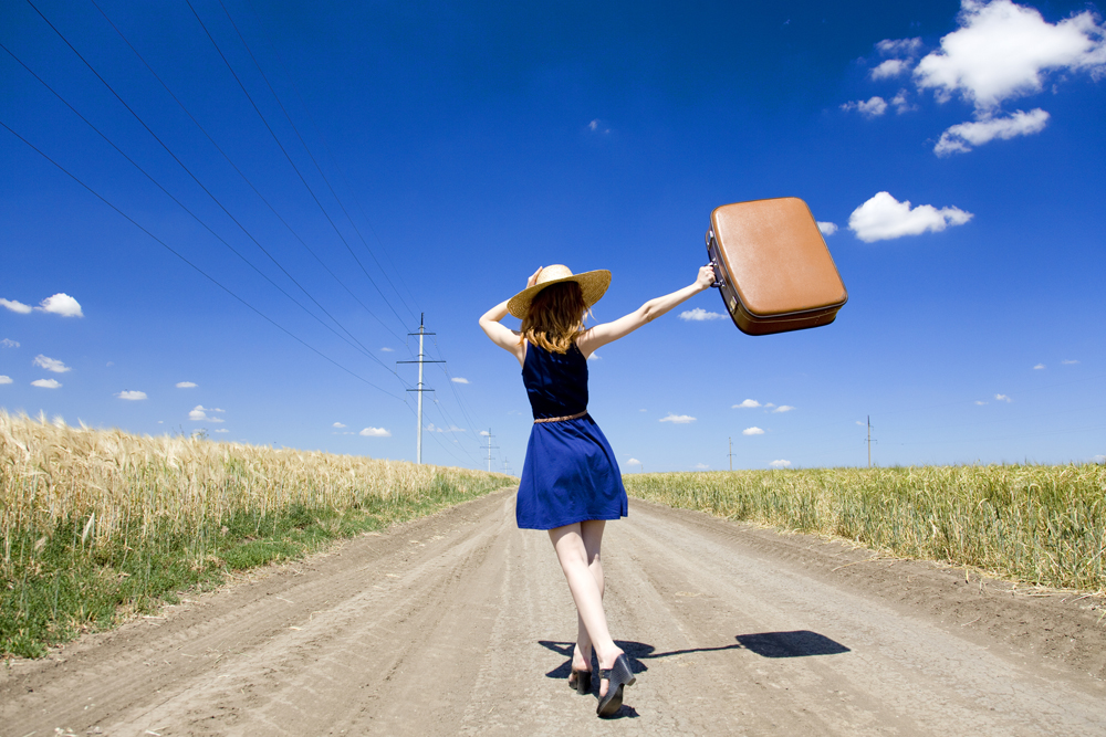 Lonely girl with suitcase at country road.